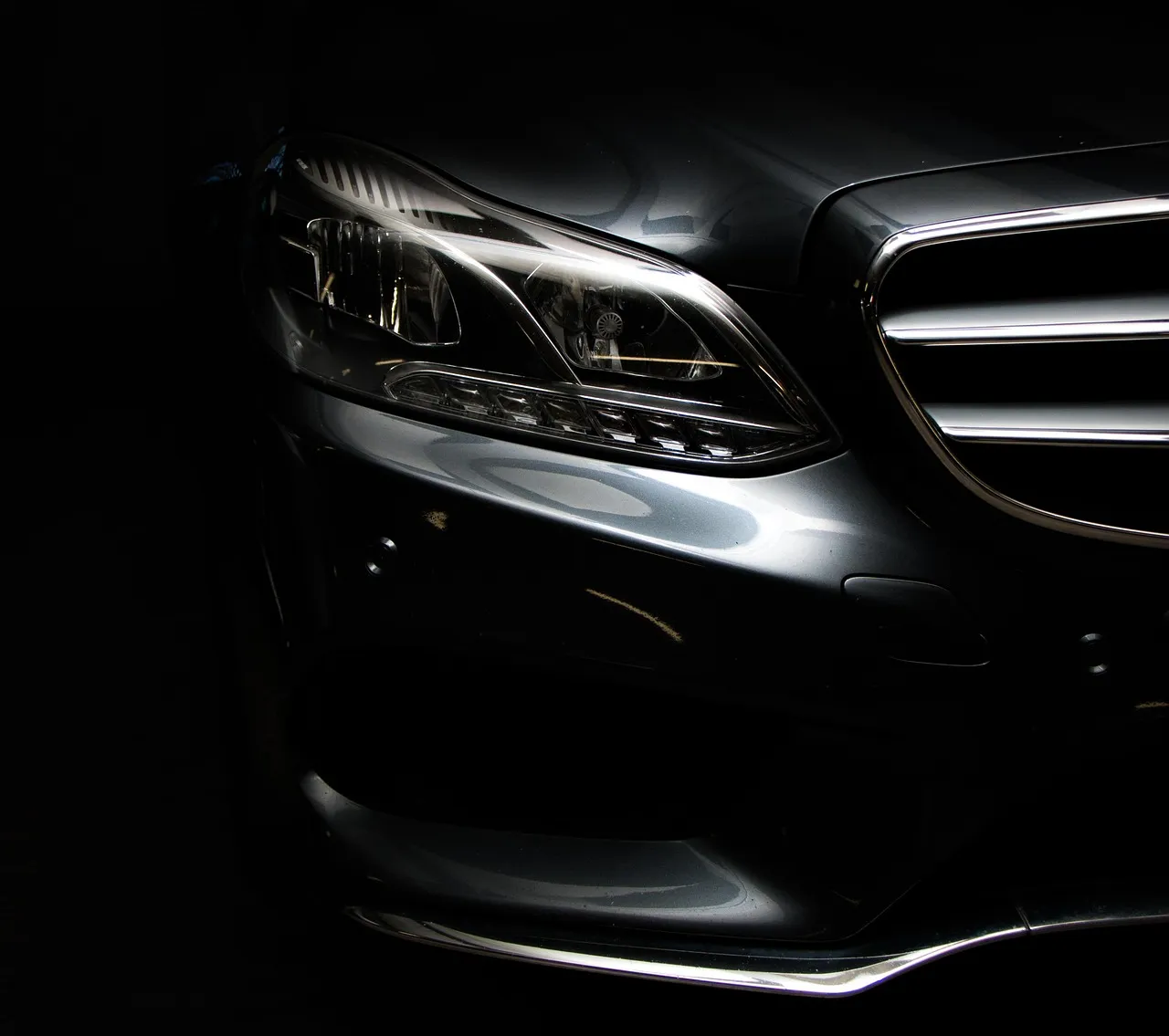 Front grille and headlight of a dark luxury car in low light